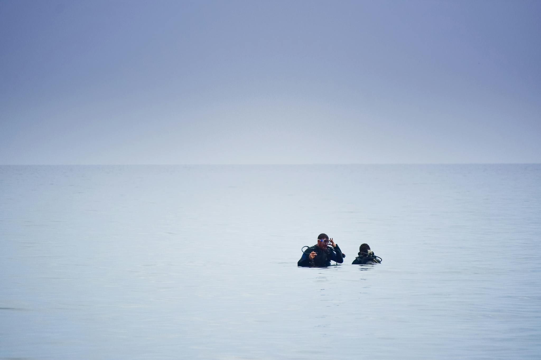 Two scuba divers in serene ocean, enjoying a tranquil dive under a clear blue sky.